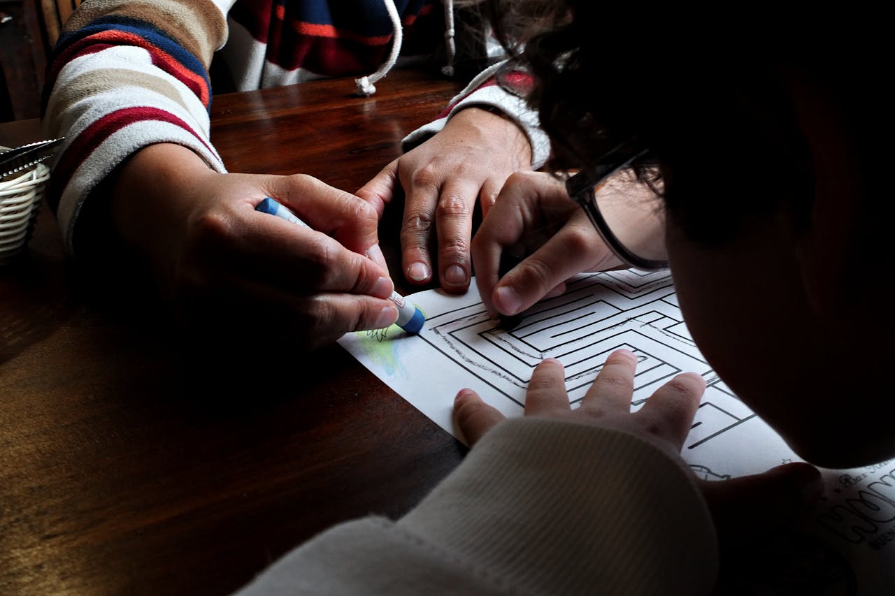 Close-up of a child solving a maze puzzle with assistance, indoors lighting, encouraging learning activity.